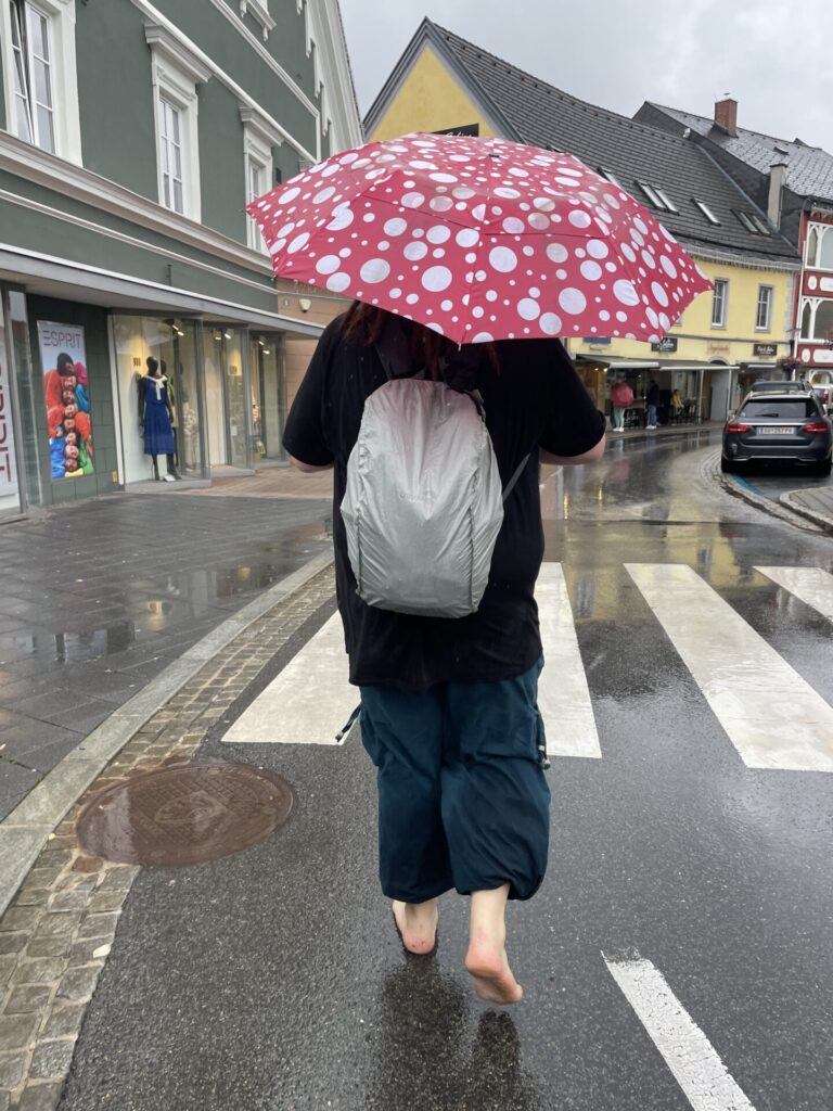 dreadhead it polka dots schirm in rot weiss im regen barfuss auf einer befahrenen strasse in österreich 